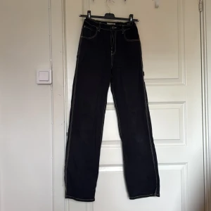 Svarta cargopants från Lindex, stl 170 - Svarta cargopants från Lindex med kontrasterande vita sömmar. Byxorna har flera fickor, inklusive bakfickor och benficka, samt breda ben och hög midja. Materialet är jeans och passformen är loose för en avslappnad vibe.