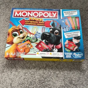 Monopoly Junior Elektronisk Bank - Monopoly Junior med elektronisk bank, komplett med spelplan, bankkort, figurer och tillbehör. Passar barn från 5 år. Alla delar syns i gott skick, inga synliga defekter. Perfekt familjespel med modern twist på klassikern.