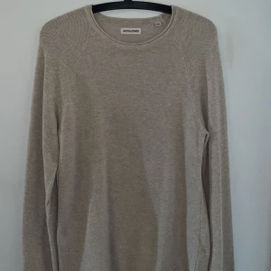 Beige stickad tröja från Jack & Jones - Säljer en stilren beige stickad tröja från Jack & Jones. Tröjan har rund halsringning och lång ärm, perfekt för lager-på-lager. Materialet är mjukt och ger en avslappnad men snygg look. Passar dig som gillar enkel och clean stil.