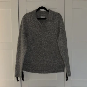 Grå stickad polotröja These Glory Days - Mysig grå stickad polotröja från These Glory Days. Tröjan har en klassisk krage med v-ringad öppning och långa ärmar. Perfekt för kyliga dagar, alpacka bomull! Nypris 1500kr