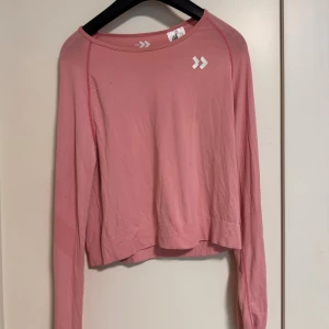 Rosa långärmad träningströja lager157 - Säljer en rosa långärmad träningströja från lager157 med vita logodetaljer på bröstet. Tröjan har en rund halsringning och är tillverkad i ett lätt och stretchigt material som passar perfekt för träning eller sportiga dagar.