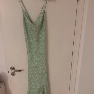 Adoore, Mintgrön blommig långklänning - Superfin mintgrön långklänning med vita små blommor, tunna axelband och snygg snörning i ryggen. Klänningen har en smickrande v-ringning och är perfekt för varma dagar. 