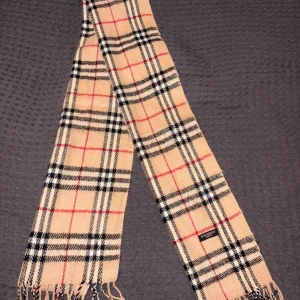 Burberry halsduk beige  - Säljer min burberry halsduk jag fick av mormor. Den köptes 2014 i london så har ej kvar kvitto. Passar bra inför den kalla säsongen och lyfter din outfit med det klassiska burberry mönstret.