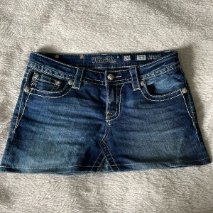 Miss Me jeanskjol med broderade fickor - Säljer en blå jeanskjol från Miss Me med snygga broderade kors på bakfickorna och glittriga detaljer på knapparna. Kjolen har markerade sömmar, klassisk femficksdesign och är i kort modell. Perfekt för dig som vill sticka ut lite extra!