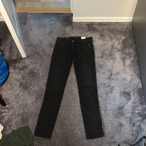 Svarta Replay Anbass jeans 31/34 - Svarta slim fit jeans från Replay, modell Anbass. Klassisk femficksdesign med svarta sömmar och diskret Replay-logga på bakfickan. Tillverkade i Italien i stretchig bomullsdenim för en bekväm passform. Perfekta för dig som gillar en stilren look.