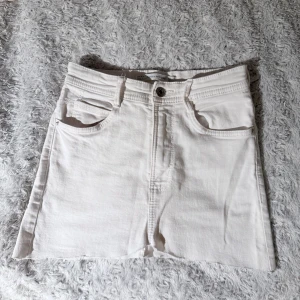 Vit jeanskjol från Zara  - Säljer en vit jeanskjol från Zara Trafaluc i klassisk denimstil. Kjolen har knapp och dragkedja framtill. Kort modell med rå kant nedtill för en cool vibe. Säljer då den inte passar längre!🩷🩷skulle säga att kjolen sitter som en XS!