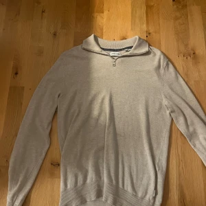 Beige halvzip-tröja från Jack & Jones - Snygg beige långärmad tröja från Jack & Jones med krage och half zip-dragkedja. Tröjan är i mjukt material och har ribbade muddar vid ärmslut och nederkant. Perfekt för lager-på-lager och stilrena outfits.