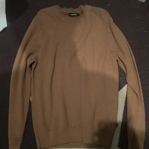 Brun stickad tröja från J.Lindeberg - Snygg brun stickad tröja från J.Lindeberg i storlek L. Tröjan har rund halsringning och långa ärmar, perfekt för lager-på-lager under hösten. Enkel och stilren design som funkar till det mesta.