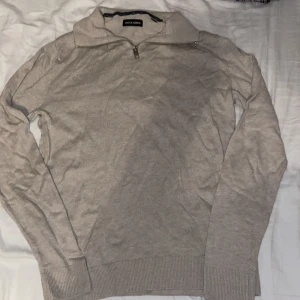 Beige half zip tröja Jack & Jones - Snygg beige långärmad tröja från Jack & Jones med half zip-dragkedja i halsen. Tröjan är stickad i mjuk bomull och har ribbade muddar vid ärmslut och nederkant. Perfekt för lager-på-lager och chill stil.