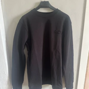 Svart Louis Vuitton sweatshirt XL - Svart sweatshirt från Louis Vuitton i storlek XL. Tröjan har ett stort lasrat LV-logo på ryggen och mindre broderade detaljer framtill. Rund hals och långa ärmar, tillverkad i mjuk bomull. Perfekt för dig som gillar exklusiva streetwear-vibes.