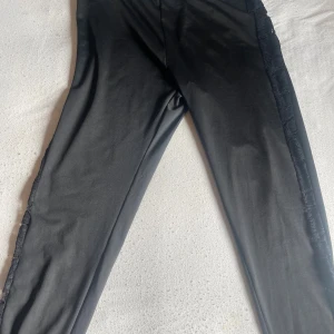 Svarta byxor med spetsdetalj - Svarta byxor stretch och snygg spets längs sidorna. Materialet är mjukt och stretchigt, vilket gör dem bekväma att bära. Perfekta för dig som vill ha en stilren look med en twist. Passar till många olika outfits.