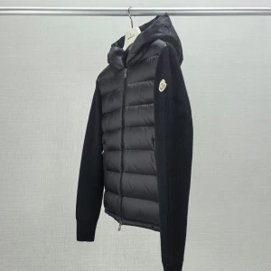 Svart Moncler cardigan med huva - Svart cardigan från Moncler med stickade ärmar och vadderad front. Jackan har huva, dragkedja framtill och Moncler-logga på ärmen. Finns i olika storlekar och i grön vill du ha mer bilder på tagg och liknande tveka inte att skriva 
