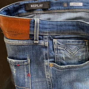 Replay Anbass blå jeans herr 33/32 - Säljer ett par Replay Anbass jeans i klassisk blå tvätt med slitningar och snygga detaljer. Modellen har smal passform och normal midja. Jeansen är tillverkade i bomull och har en skinnpatch bak i midjan. Perfekta för dig som gillar en modern och avslappnad look.