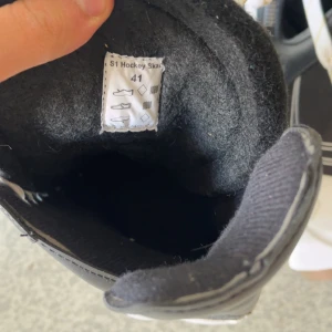 Svarta hockeyskridskor från Head strl 41 - Säljer ett par svarta och vita hockeyskridskor från Head i storlek 41. Skridskorna har snörning, robust design och är fodrade för extra komfort. Perfekta för dig som vill glida fram på isen med stil. Klassisk look med vita detaljer och slitstark syntet på ovandelen.