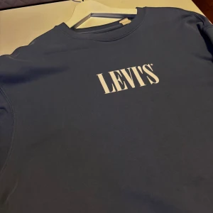Blå sweatshirt från Levis - Säljer en stilren blå sweatshirt från Levi's med klassisk vit logga på bröstet. Tröjan har rund halsringning och långa ärmar. Passar L/M.