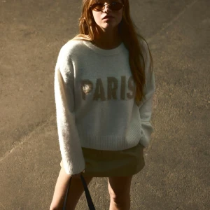 Vit stickad tröja med PARIS-tryck - Supermjuk vit stickad tröja från h&m med stora beiga bokstäver 'PARIS' framtill. Tröjan har rund hals, ribbade muddar och en lite loose passform. Perfekt för dig som gillar chill och trendig stil.