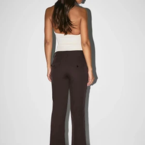 Bruna bootcut kostymbyxor - Snygga bruna kostymbyxor med bootcut-snitt och klassiska bakfickor med knapp. Byxorna har en elegant och tidlös look, perfekta för dig som gillar stilrena och trendiga outfits. Passar dig som vill ha en modern siluett med lite utsvängda ben.