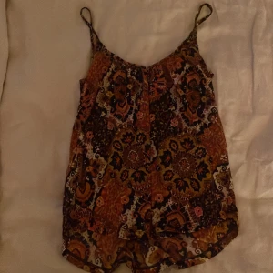 Mönstrad linnetopp från H&M - Säljer en färgstark linnetopp från H&M med tunna axelband och ett bohemiskt blommigt mönster i orange, brun, svart och rosa. Toppen är lätt och luftig, perfekt för varma dagar. Materialet är mjukt och skönt mot huden.