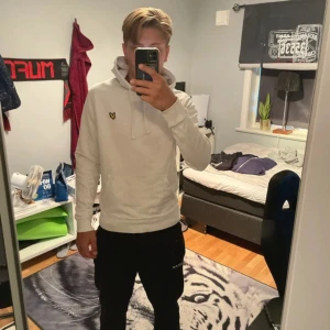 Vit hoodie från Lyle & Scott - Säljer en stilren vit hoodie från Lyle & Scott med klassisk gul logga på bröstet. Tröjan har huva med snörning och är långärmad. Perfekt för dig som gillar enkel och clean streetstyle.