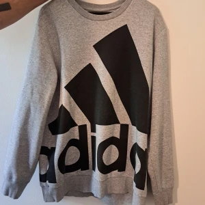 Grå Adidas sweatshirt XL - Säljer en grå sweatshirt från Adidas i storlek XL med stort svart logotryck över hela framsidan. 