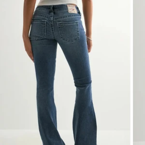 Blå bootcut jeans från True Religion - Snygga blå jeans från True Religion med klassiska kontrastsömmar och ikoniska bakfickor. Modellen har bootcut-ben och normal midja. Jeansen är tillverkade i denim med lätt tvättad look och har knapp- och dragkedjegylf.