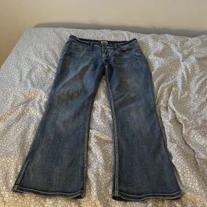 blå bootcut jeans - Snygga jeans i klassisk blå tvätt med bootcut passform. Jeansen har fem fickor, bälteshällor och dragkedjegylf. Perfekta för dig som gillar en retro vibe och vill ha ett par jeans med lite vidare ben. Materialet är slitstarkt denim.