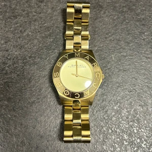 Marc Jacobs MBM3126 - Stilren klocka från Marc Jacobs i helguldigt utförande med länkarmband i metall. Urtavlan är enkel och elegant med märkets logga runt boetten. Jättelite slitage på baksidan. Perfekt accessoar för dig som gillar en lyxig och modern look. Batterier behöver bytas ut, kostar inte mer än 200-250 kr.