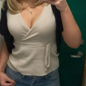 Beige omlottopp med knyt i midjan - Säljer en beige omlottopp med v-ringning och knyt i midjan. Toppen har korta ärmar och är tillverkad i ett mjukt material som sitter snyggt på kroppen. Perfekt att styla med jeans för en trendig look.