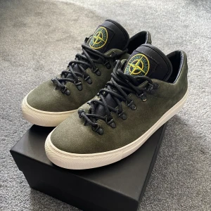 Stone Island gröna mockasneakers - Snygga sneakers från Stone Island i olivgrön mocka med svart plös och tydlig ikonisk logga på tungan. Skorna har svarta snören med metalltippar och vita sulor.  Ny pris 4499kr Mitt Pris 2800kr