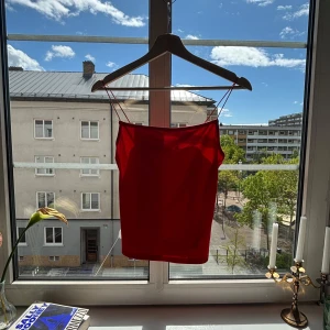 Röd linnetopp med tunna axelband - Snygg röd linnetopp med spagetti axelband och rak skärning. Perfekt för varma dagar och enkel att styla med jeans eller kjol. Toppens material känns mjukt och följsamt mot huden och ger en clean look. Använd en gång! 