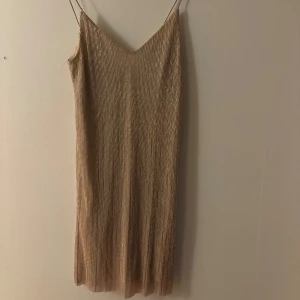 Glittrig champagneklänning Gina Tricot - Supersnygg glittrig kortklänning från Gina Tricot i champagnefärg. Klänningen har tunna axelband, v-ringning och ett skimrande tyg med vertikala ränder. Perfekt för dig som vill sticka ut med en elegant och trendig look.