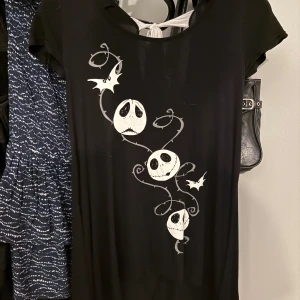 Svart T-shirt med Jack Skellington - Svart T-shirt med tryck av Jack Skellington och vita fladdermöss framtill. T-shirten har korta ärmar, djup rygg med knytband i vit och coola detaljer som slingrande mönster. Perfekt för dig som älskar Nightmare Before Christmas! Köpte på Plick men har aldrig använt!