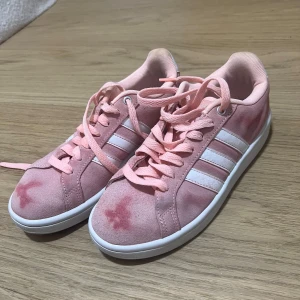 Rosa Adidas sneakers med mocka - Snygga rosa sneakers från Adidas med klassiska vita ränder på sidorna. Skorna har snörning och är tillverkade i mjuk mocka med platt sula och rund tå. Perfekta för dig som gillar sportig och trendig stil. Missfärgning är pga tvättat.