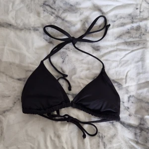 Svart trekantsbikini överdel med knyt - En stilren svart trekantsbikini från lager 157 med tunna knytband i nacken och ryggen. Klassisk modell med justerbara band och mjukt, stretchigt material som sitter skönt. Perfekt för stranden eller poolen. Är aldrig använd. Jag säljer den för att jag beställde en för liten storlek