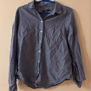 Blå bomullsskjorta från Gina Tricot - Klassisk blå skjorta från Gina Tricot i mjuk bomull. Skjortan har långa ärmar, vit knappstängning framtill och en tidlös krage. Perfekt för en avslappnad men ändå stilren look.