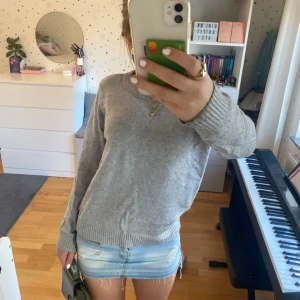 Grå stickad tröja med rund hals - Mysig grå stickad tröja med rund halsringning och ribbade muddar vid ärmslut och nederkant. Perfekt för lager-på-lager och enkel att matcha med olika outfits. Klassisk och stilren design som funkar året runt.