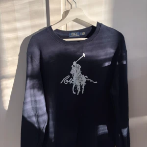 Mörkblå tröja från Polo Ralph Lauren - Mörkblå sweatshirt från Polo Ralph Lauren med stort vitt polospel-tryck på bröstet. Klassisk rund halsringning och långa ärmar. Perfekt för dig som gillar stilrena och sportiga plagg med ikonisk logga. Storlek XL men sitter som M/L