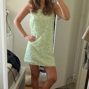 Ljusgrön blommig kort klänning - Superfin ljusgrön kort klänning med tunna axelband och blommigt mönster i vitt och gult. Klänningen har rak passform och är perfekt för varma dagar. Materialet känns lätt och luftigt, och den har en söt, somrig vibe.