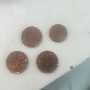 Svenska mynt, 1 och 2 kronor - Fyra svenska mynt i kopparfärg: tre 2-kronorsmynt och ett 1-kronorsmynt. Mynten är i gott skick med mindre spår av användning. Perfekt för samlare eller som växel. Årtal och motiv tydligt synliga.