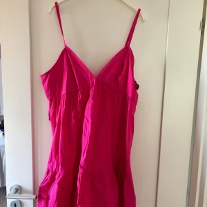 Rosa kortklänning med smala axelband - Säljer en superfin rosa kortklänning med smala axelband och v-ringning. Klänningen har en luftig passform och snygga volangdetaljer nedtill. Baksidan har en öppen rygg med justerbara band som gör att även storleken är justerbar!  Knappt använd och tyvärr har lappen försvunnit men skulle säga att det är en M/L då man kan justera storleken