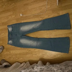 Blå bootcut jeans från SHEIN - Snygga ljusblå bootcut jeans från SHEIN med utsvängda ben och coola slitningar framtill. Baksidan har dekorativa sömmar och nitar på fickorna. Jeansen är tillverkade i bomull, polyester och elastan för en bekväm passform.