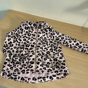 Leopardmönstrad jacka från H&M - Snygg jacka från H&M i ljusrosa med svart och rosa leopardmönster. Jackan har dragkedja framtill, två stora fickor med lock och knapp samt hög krage. Perfekt för dig som vill sticka ut med ett coolt mönster.