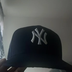 Svart New Era NY Yankees keps - Säljer en svart New Era keps med klassiskt NY Yankees broderi i vitt framtill. Kepsen har rak skärm och broderad MLB-logga bak. Perfekt för dig som gillar sportig och stilren streetwear.