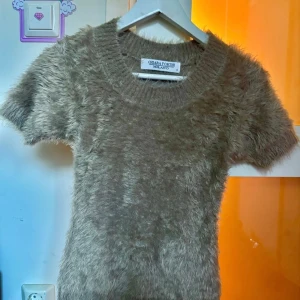 Beige fluffig tröja från Chiara Forthi - Supermjuk och fluffig beige tröja från Chiara Forthi Milano. Tröjan har korta ärmar, rund halsringning och är tillverkad i ett pälsliknande material som ger en unik look. Perfekt för dig som vill sticka ut med en cozy vibe.