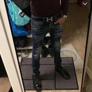 Dsquared2 ICON slim fit jeans blå - Säljer ett par Dsquared2 ICON jeans i mörkblå tvätt med slitningar och färgstänk. Slim fit med klassiska fem fickor och röd Dsquared2-tag fram. Snyggt blekta partier och stor röd ICON-patch bak. 