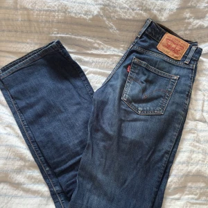 Levi's 505 blå jeans bootcut - Säljer ett par klassiska Levi's 505 jeans i mörkblå tvätt med bootcut passform. Jeansen har fem fickor, orange sömmar och ikonisk läderpatch bak. Perfekt för dig som gillar retrovibe och schysst kvalitet. Passar dig som vill ha lite bredare ben.