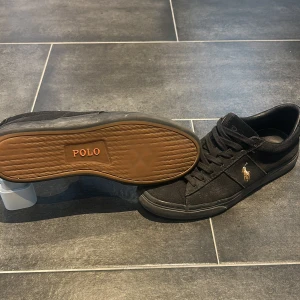 Svarta sneakers från Polo Ralph Lauren - Svarta sneakers från Polo Ralph Lauren med klassisk låg profil, snörning och gummisula. Ett litet hål på sidan av en utav skorna, använts många gånger men håller annars ett hyfsat skick, ord pris ligger på 1,500, 