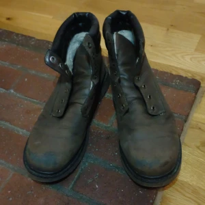 Bruna fodrade boots i skinn - Rejäla bruna boots med högt skaft och svart vadderad kant upptill. Skorna är fodrade med ljust foder och har grov sula. Tillverkade i skinn och passar perfekt för kyligare dagar. Klassisk design med plats för snörning.