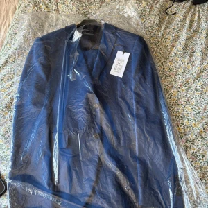 Blå super slim kostym från Jack & Jones - Snygg blå kostym från Jack & Jones i super slim passform. Kavajen har klassisk design med två knappar, fickor fram och slät yta. Materialet är polyester och kostymen har svarta detaljer på insidan. Perfekt för dig som gillar stilren och modern look.