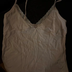 Linne med spets - Söt  linnetopp med smala axelband och v-ringning dekorerad med spets. I fint skick.